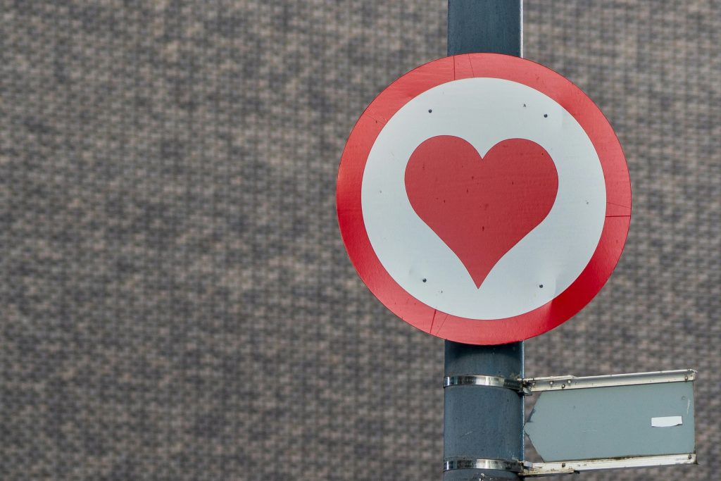 A circular roadsign with a red heart on a white background