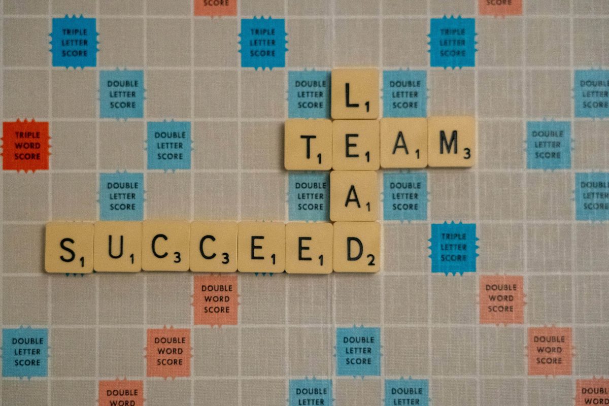 A scrabble board with the letter tiles spelling the words lead, team and succeed