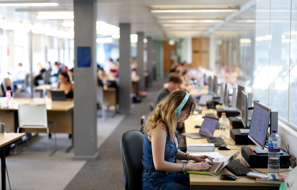 Students studying with laptops at desks in a library space.